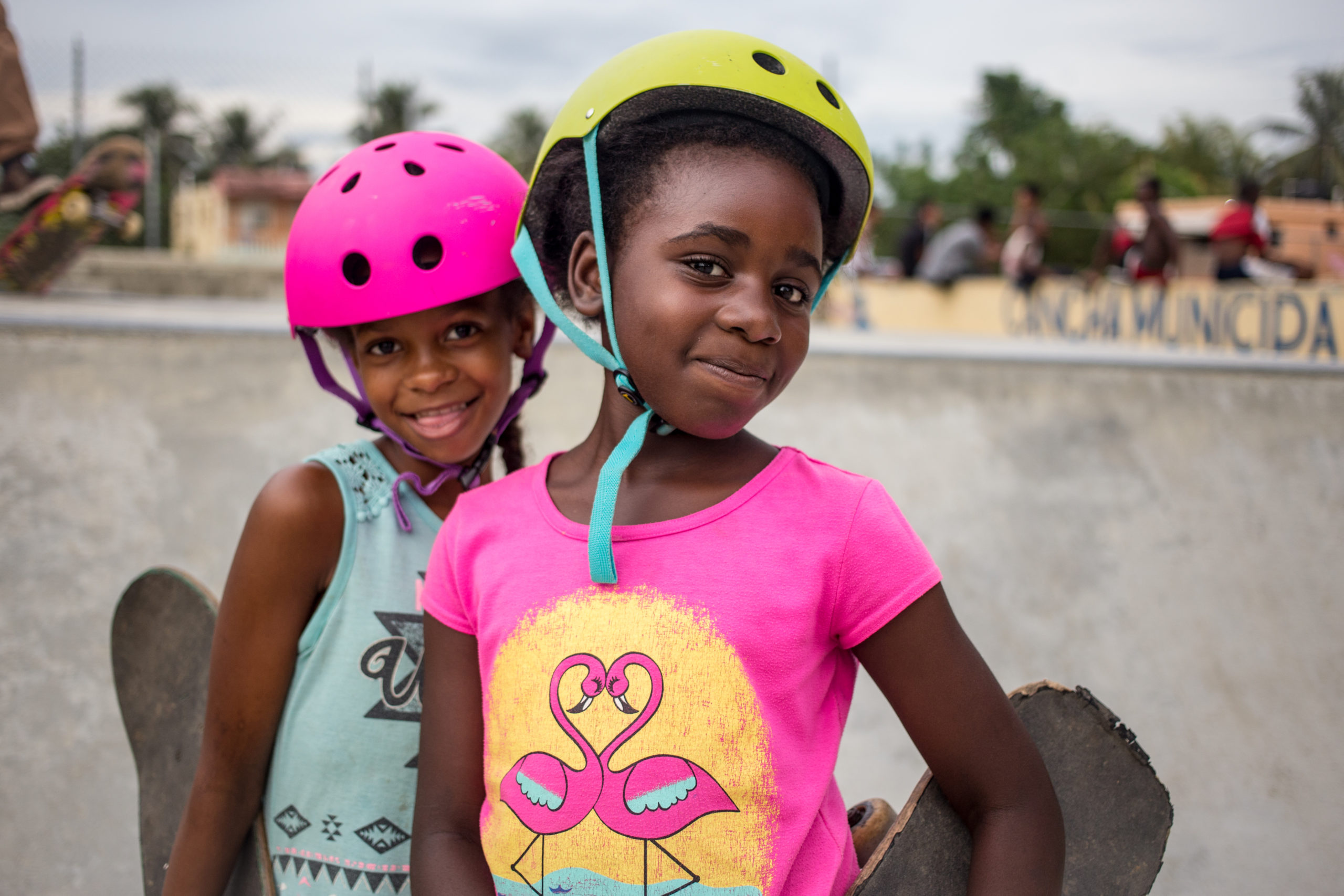 two girls in helmets, smiling and holding their skateboards