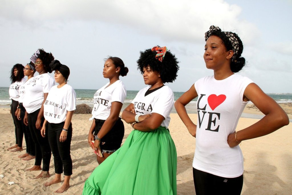 Women stand in a line on a beach looking off into the distance