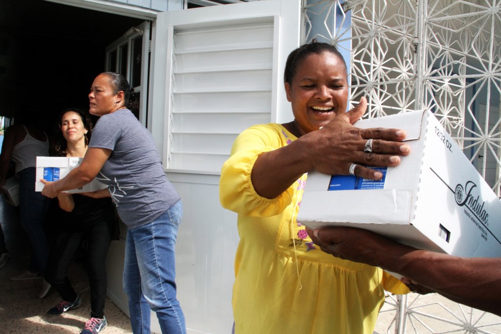 A woman hands off a box of supplies in the foreground while women pass boxes in the background