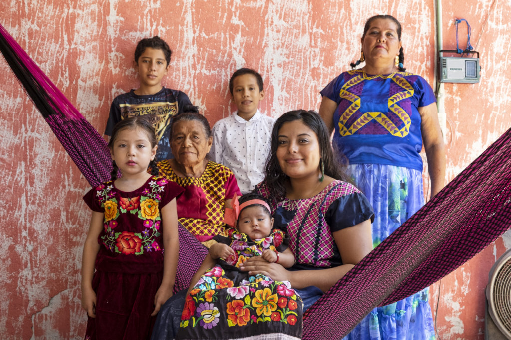 A woman sits on a hammock surround by her children and family
