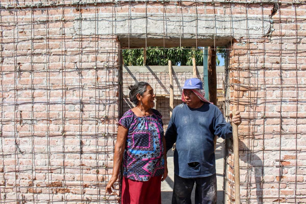 A woman and a man stand in the doorway of a home with exposed bricks and rebar. 