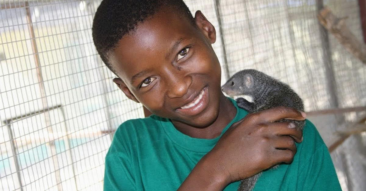 Young boy holding a baby mongoose; A part of DAKTARI's innovative education program teaching local kids about animals and the environment.