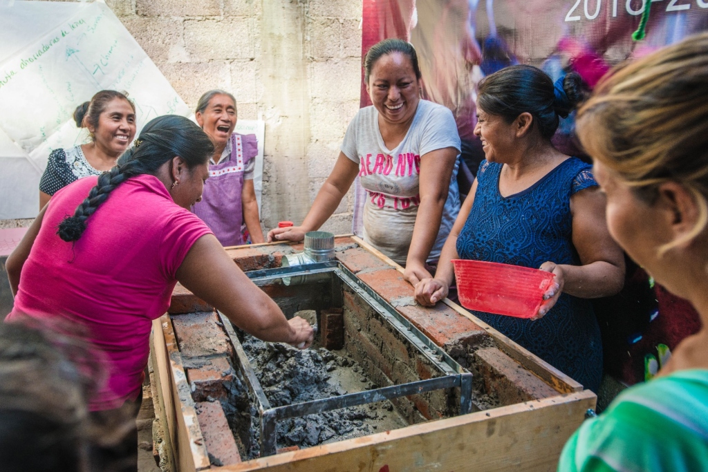 A group of women laugh while rebuilding an oven with bricks and cement.