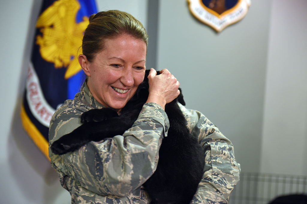 Woman in military uniform hugs black lab puppy. Dogs with jobs helping veterans and service members.