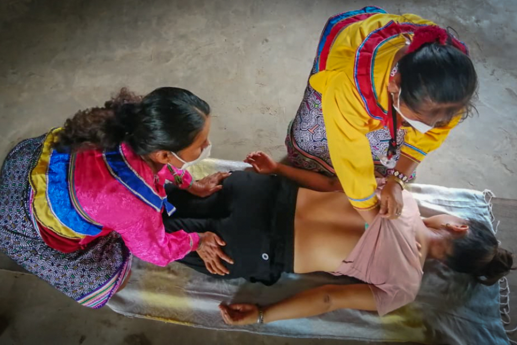 Two women perform a healing massage another woman laying down on her stomach.