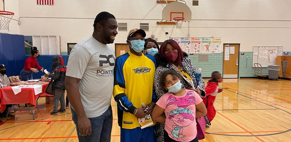 A family and nonprofit staff wearing face masks stand in a gymnasium