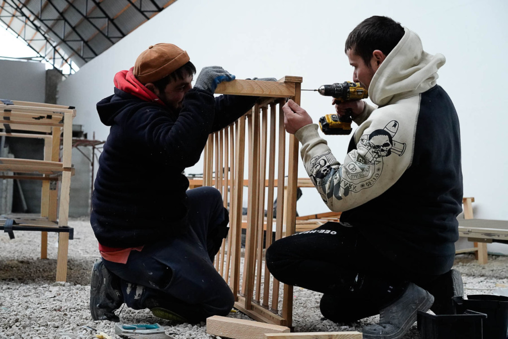Two people put together a bed frame with a screwdriver on the floor. Nonprofits helping Ukraine. 