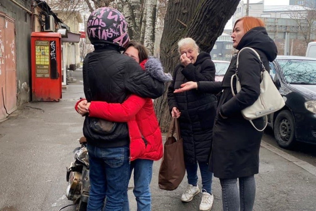 A young woman hugs a man wearing a jacket and motorcycle helmet. Two older women stand near them. One is wiping tears from her eyes. Nonprofits helping Ukraine.