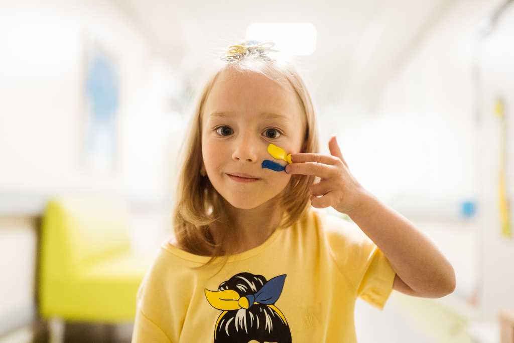 Young girl paints her cheek with blue and yellow of the Ukrainian flag