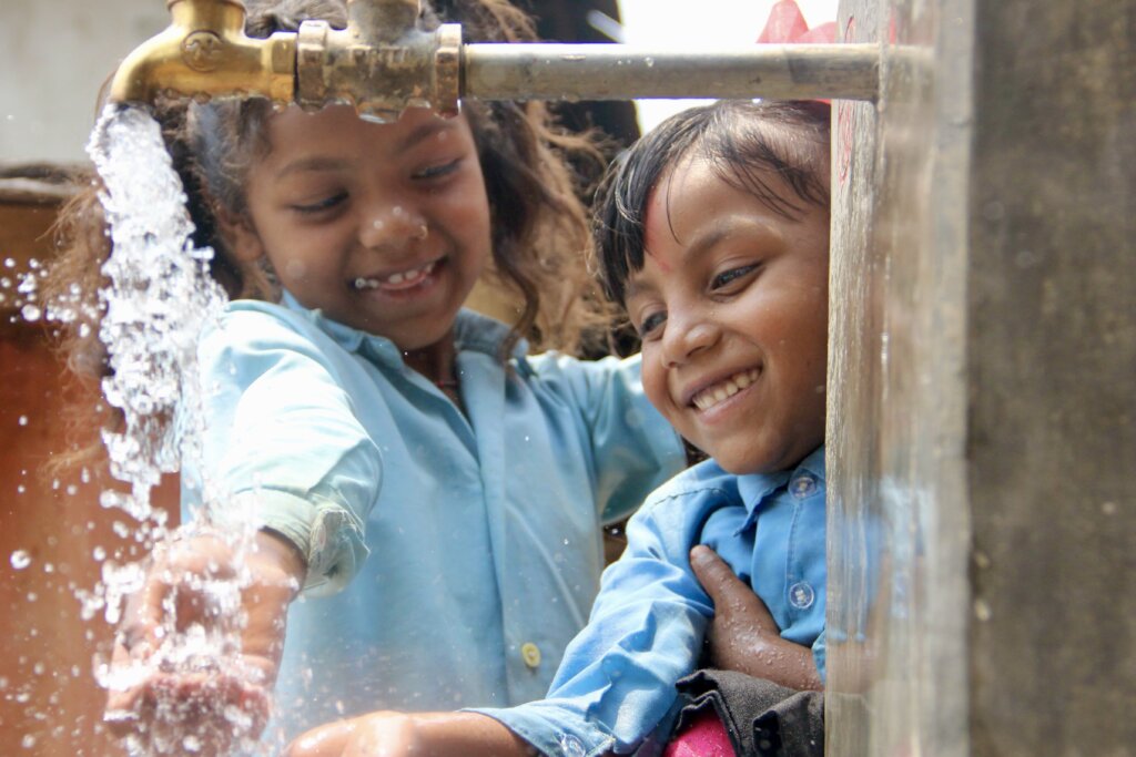 Two kids catch water from a faucet, smiling - photos of 2022