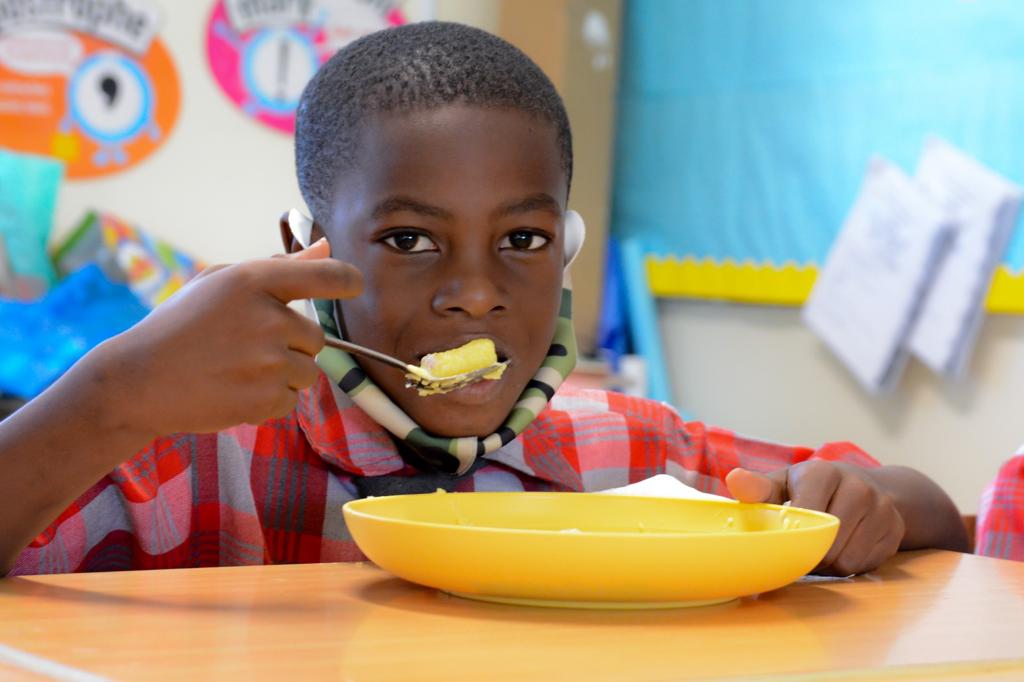 Boy lifts a spoon of food to his mouth as he looks at the camera