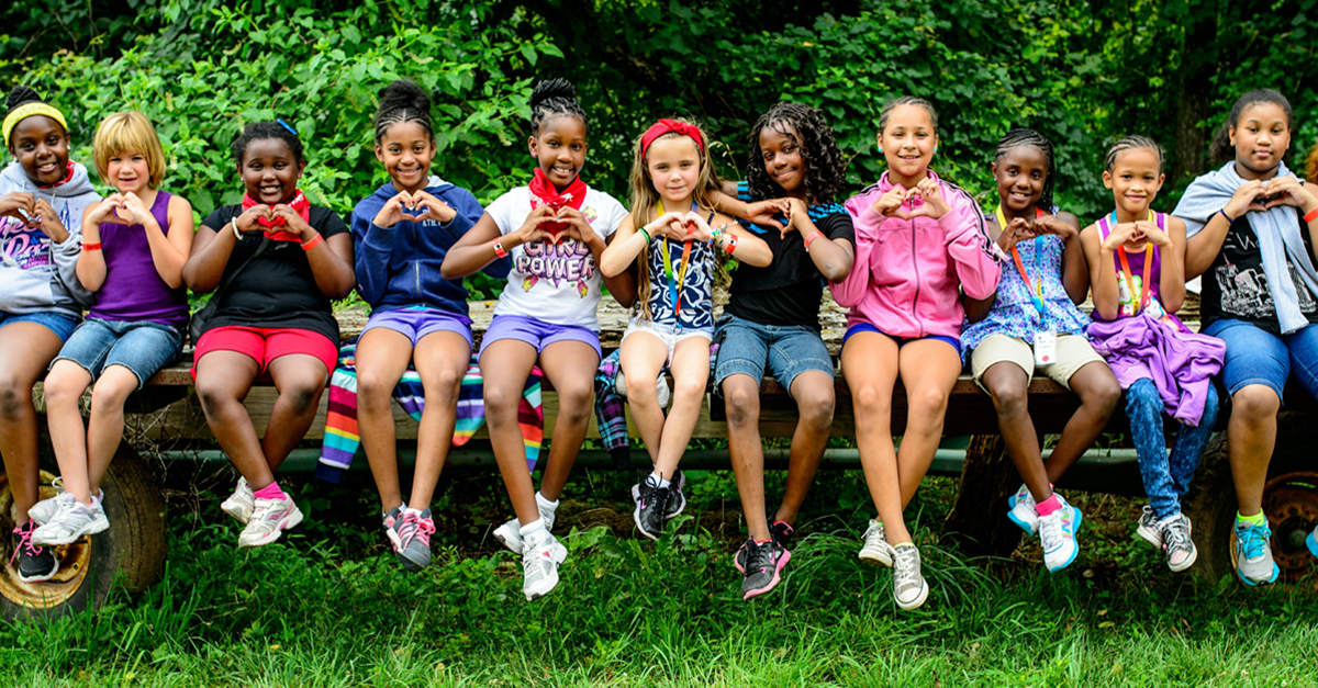 compassionate child. Smiling kids sit next to each other on a bench and make heart signs with their hands