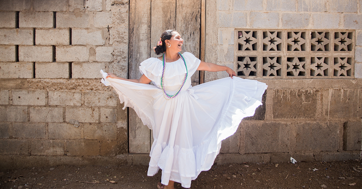 A woman in a white dress dancing in front of a brick building. Employee happiness