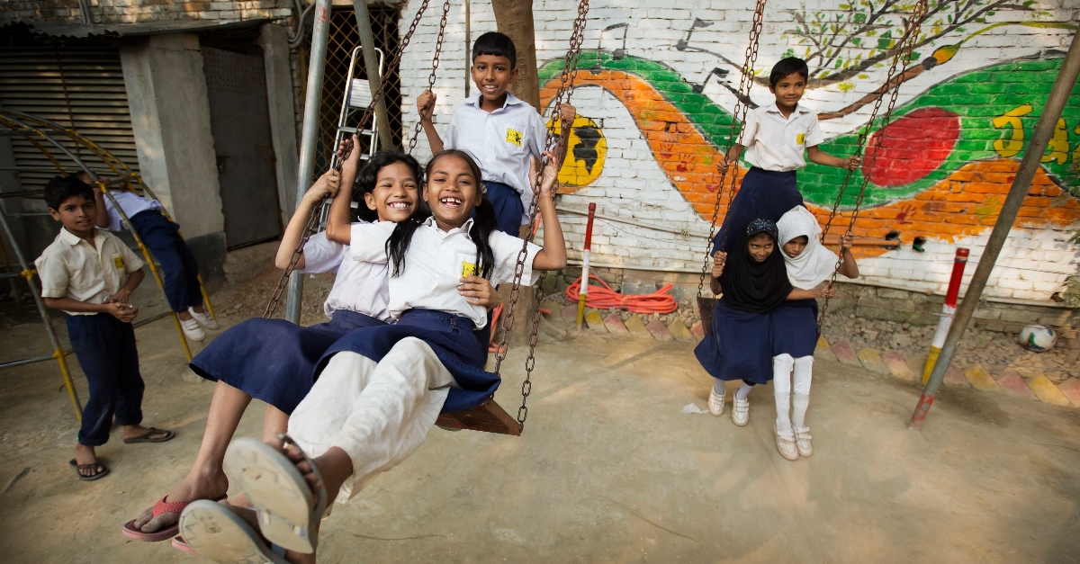Students in blue and white uniforms play on swings