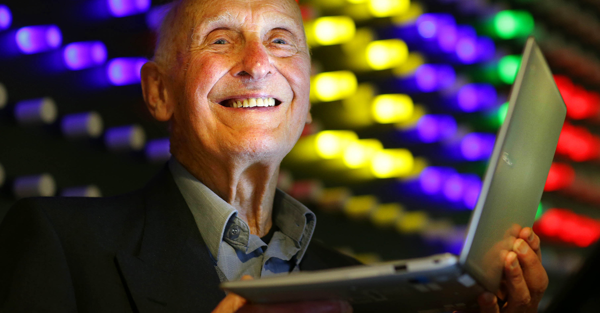 A man holding a silver laptop in front of a background of multicolored lights