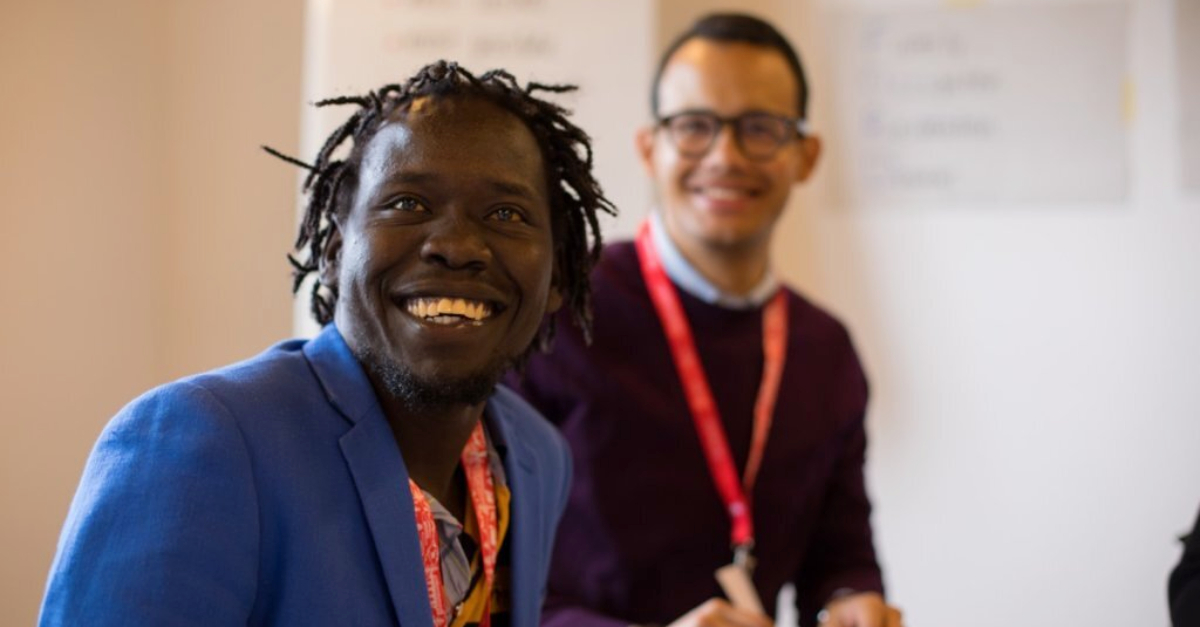 A man in a blue suit and a red lanyard smiles in the foreground