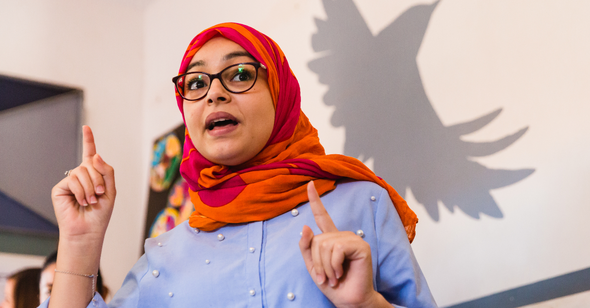 Business neutrality. A woman in a blue shirt and pink and orange hijab speaking with her index fingers raised