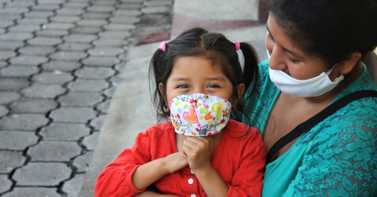 globalgiving's impact in 2020. A woman in a mask and a blue shirt holds a young girl wearing a mask and a red shirt. with her hands clasped below her chin.