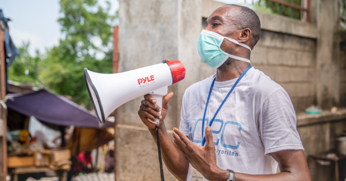 A man wearing a blue mask holding a megaphone. Covid-19 complicates disaster response