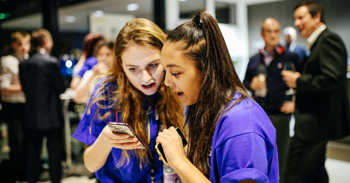 Two girls in blue shirts looking at cell phones