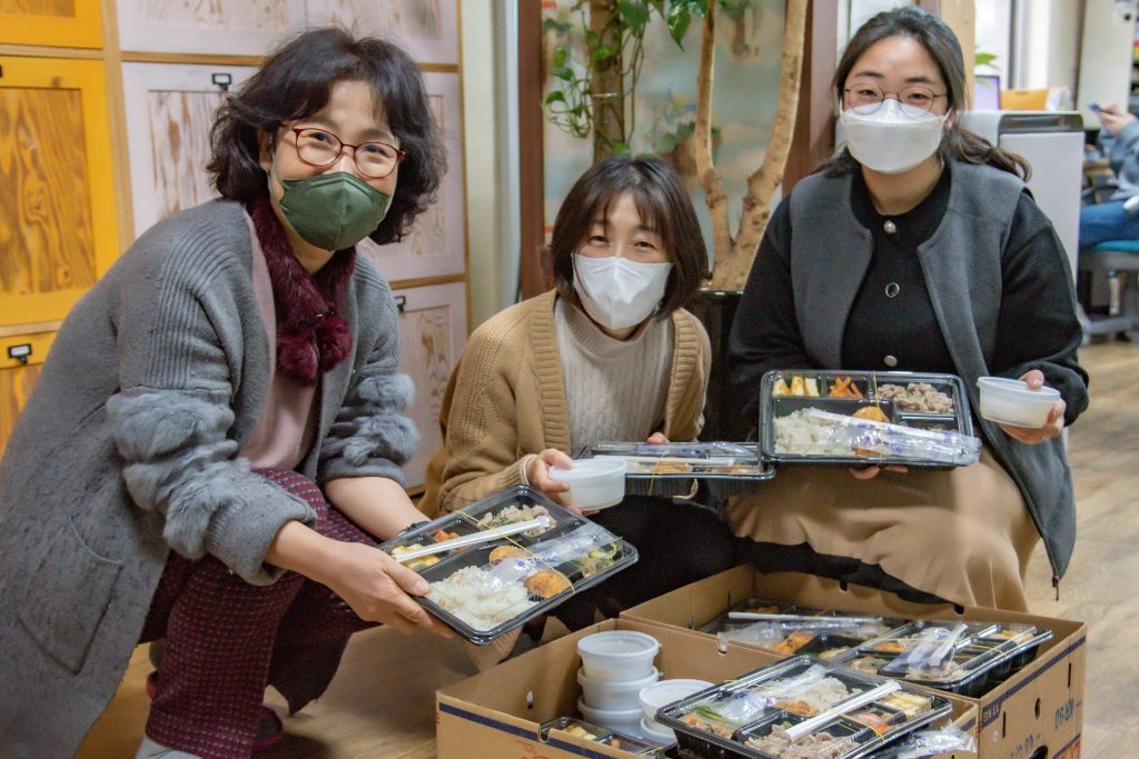 Three women in masks hold trays of food