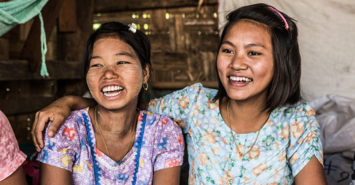One girl drapes her arm around the shoulder of another smiling girl.