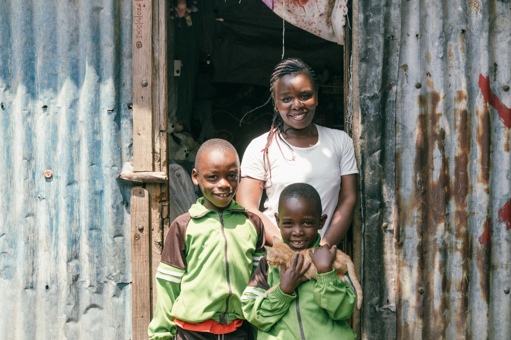 Three children stand in the doorway of a house