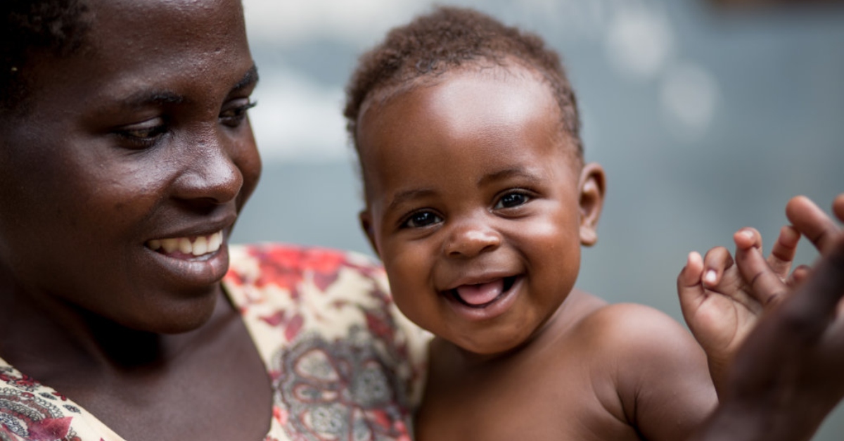 A woman holds a smiling infant who is looking straight ahead