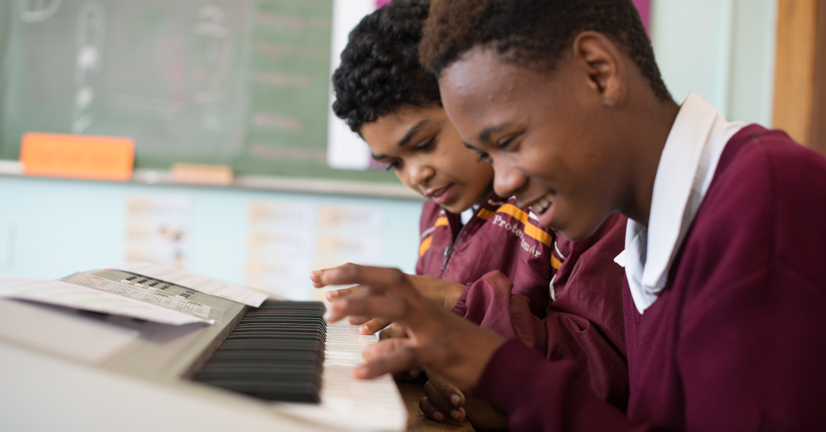 Two boys in red uniforms play a keyboard together