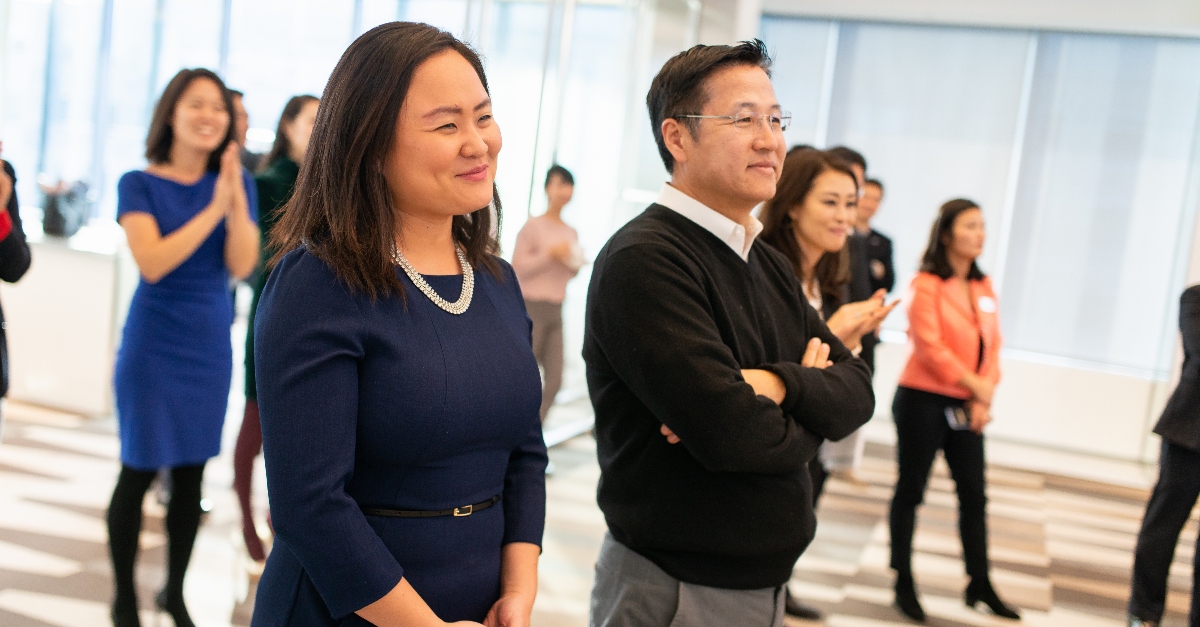 Members of the Council of Korean Americans stand together at an annual gala. One male and one female member in business attire are in the foreground.