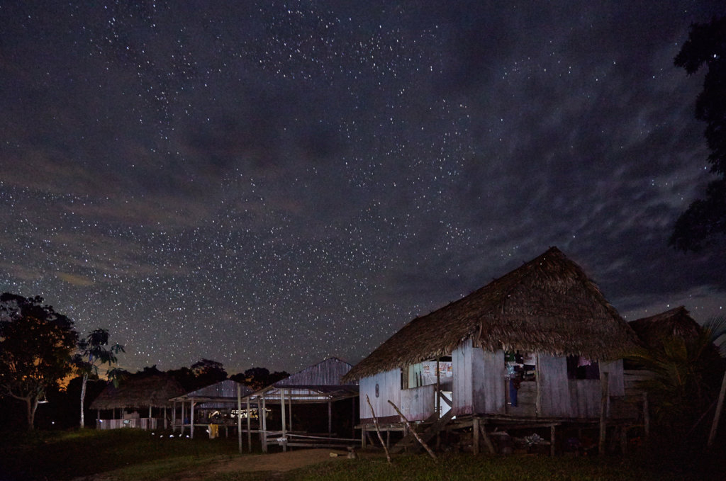 Houses in a Maijuna community are in the foreground below a starlit sky.