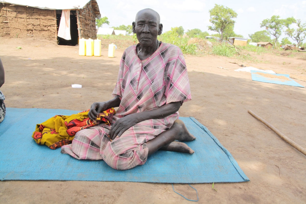 A woman in a pink patterned dress sits with her legs folded beneath her on a blue mat