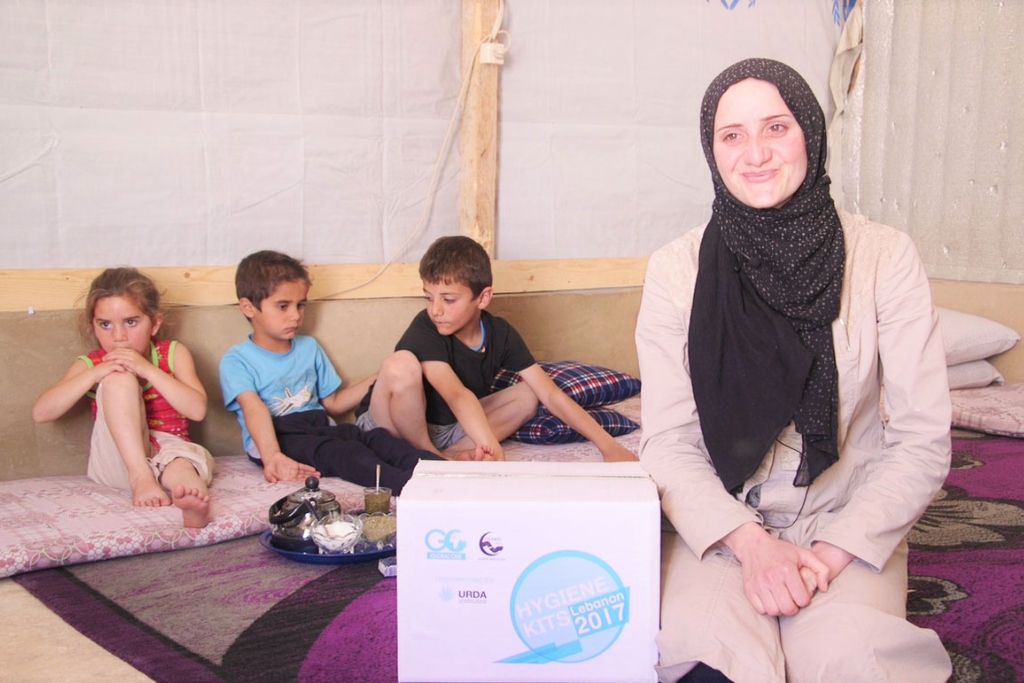 A woman in a black head covering sits on a carpet with three children behind her