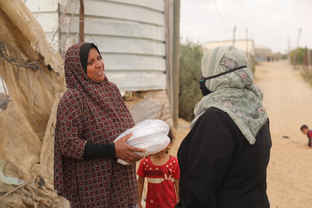 A woman with a young girl at her side smiles as she receives two containers of food from Mrs. Najah.