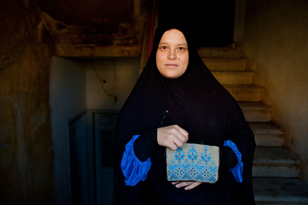 A woman in a black head covering holds a hand-sewn blue purse
