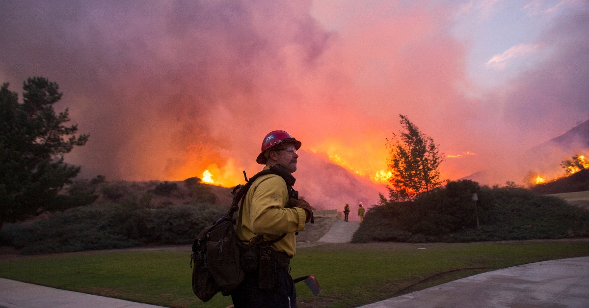 A firefighters stands with pink and orange flames behind him in the distance at the Blue Ridge Fire in Yorba Linda