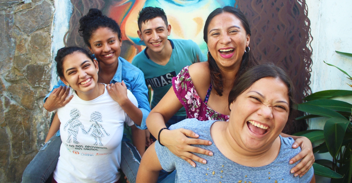 Young people smile in front of a wall mural of a woman's face