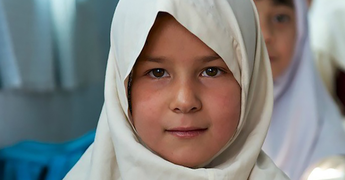 A little girl from Herat, Afghanistan, in a white hijab looks at the camera.