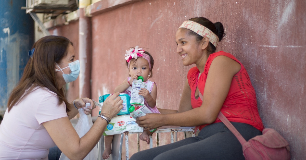 A woman and her young daughter receive children's aid supplies from Friends of the Children of Venezuela worker