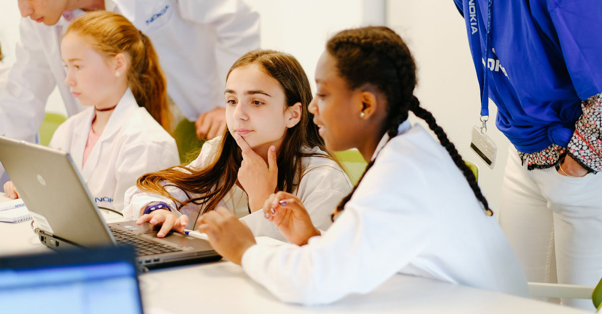 Girls with thoughtful expressions gathered around laptop learning about coding. One example of gender equality Initiatives from around the world to highlight in the new year.