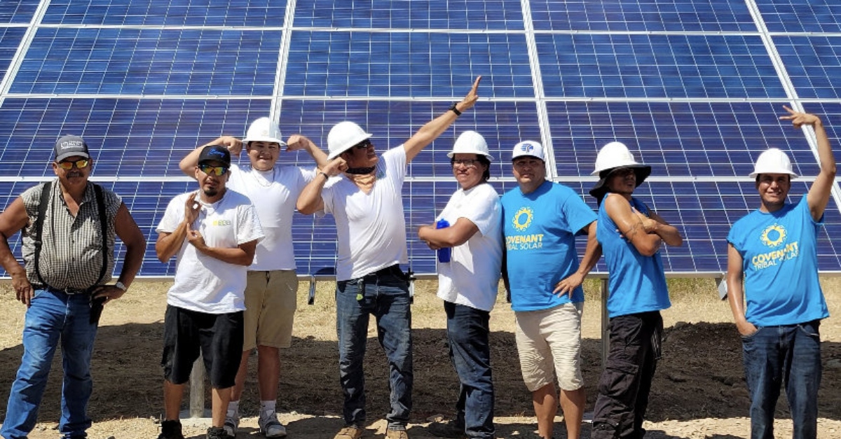 An team posing in front of a solar panel powering a community center during the Indigenous-led training program