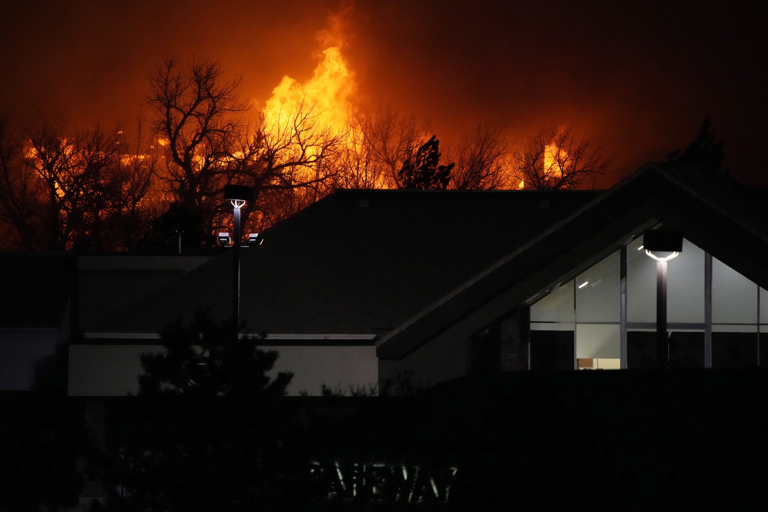 Flames from wildfires rise above and encroach on a shopping center.