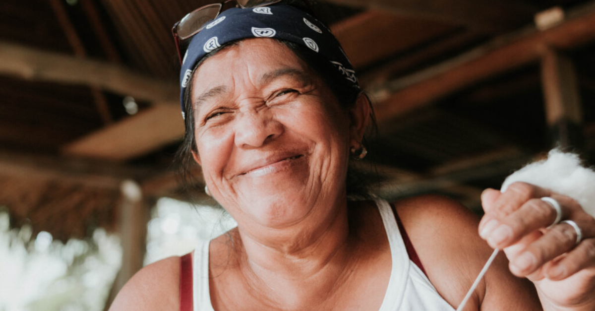 A woman wearing a blue bandana and glasses on top of her head smiles as she holds a string in her hand. Questions To Ask Before Writing A Grant Proposal