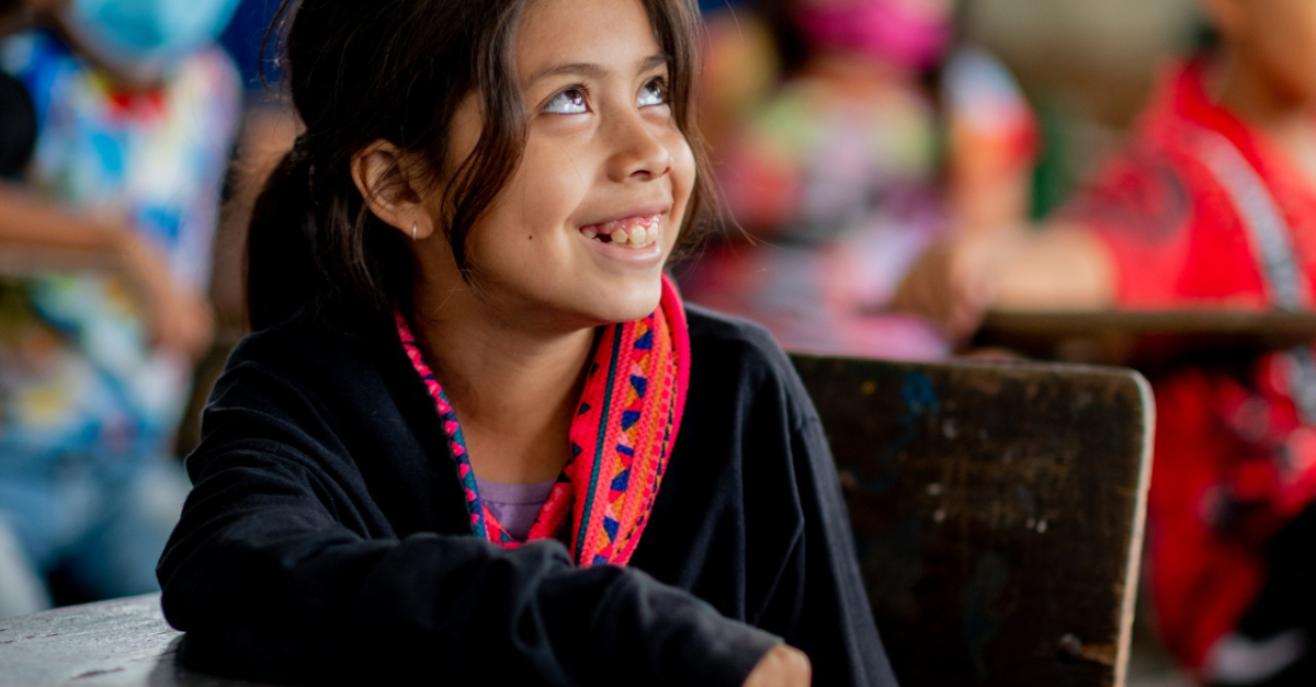 A young girl seated at a desk looks up to the right