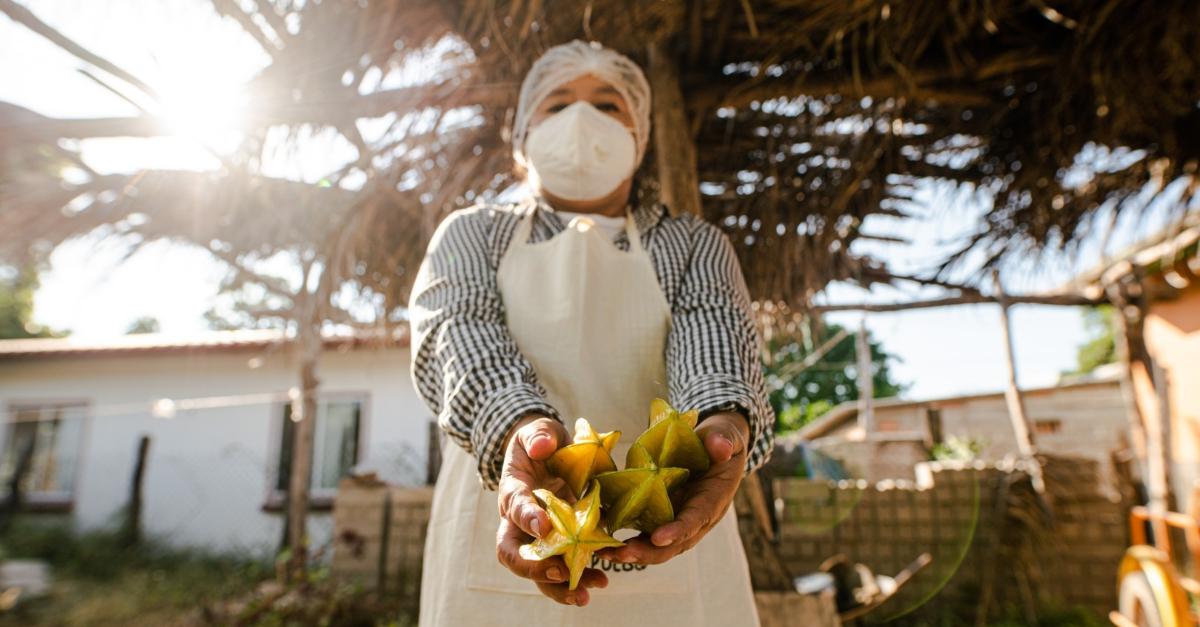 A person wearing a mask is holding star fruit.