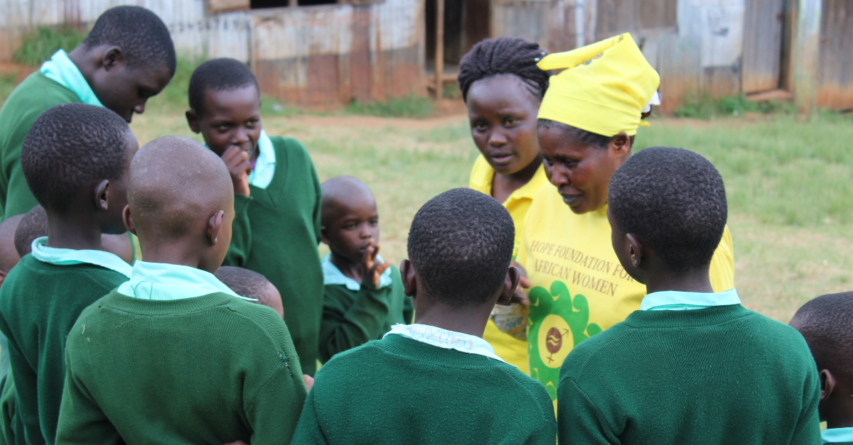Two women in yellow shirts talk with a group of students dressed in green uniforms about FGM