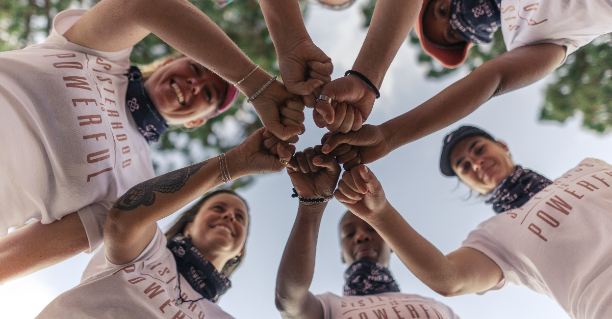 A group of people wearing pink t-shirts put their fits in a circle