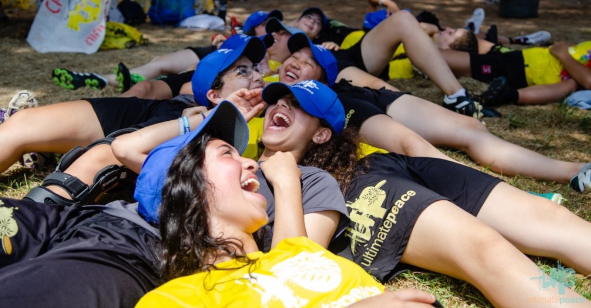 A group of young girls wearing blue hats and t-shirts laugh while laying on the ground