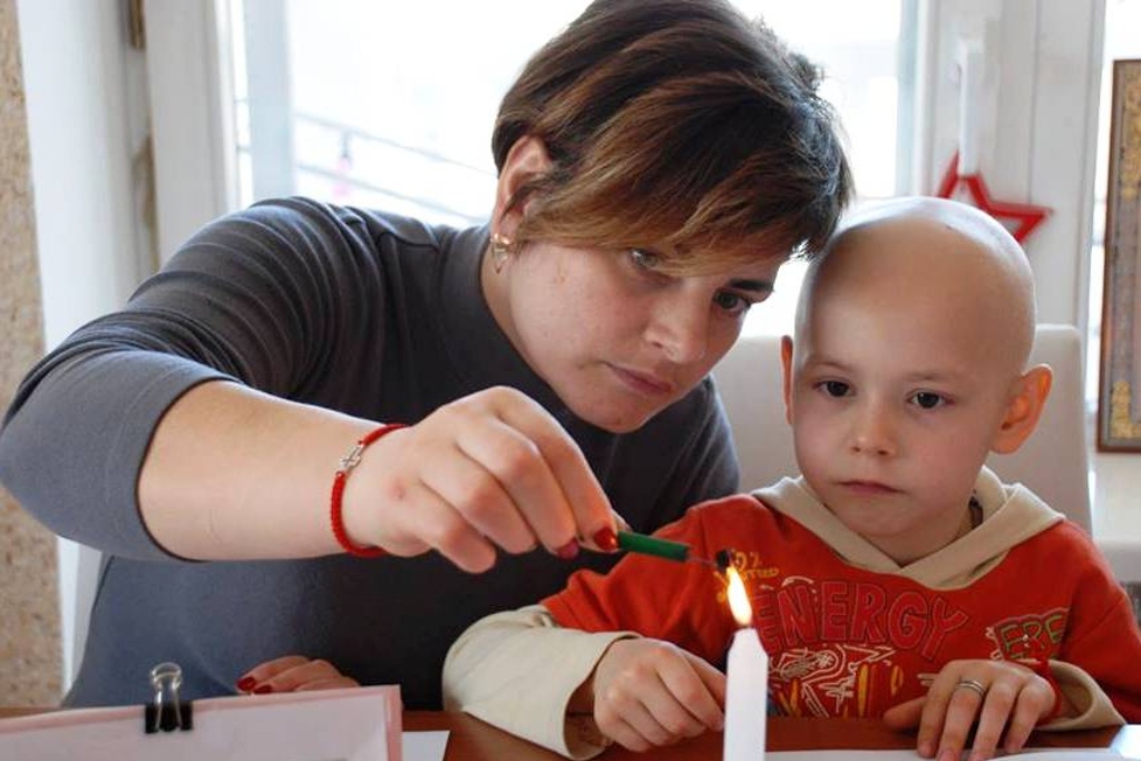 A mother and her son hold a green item near a candle flame.