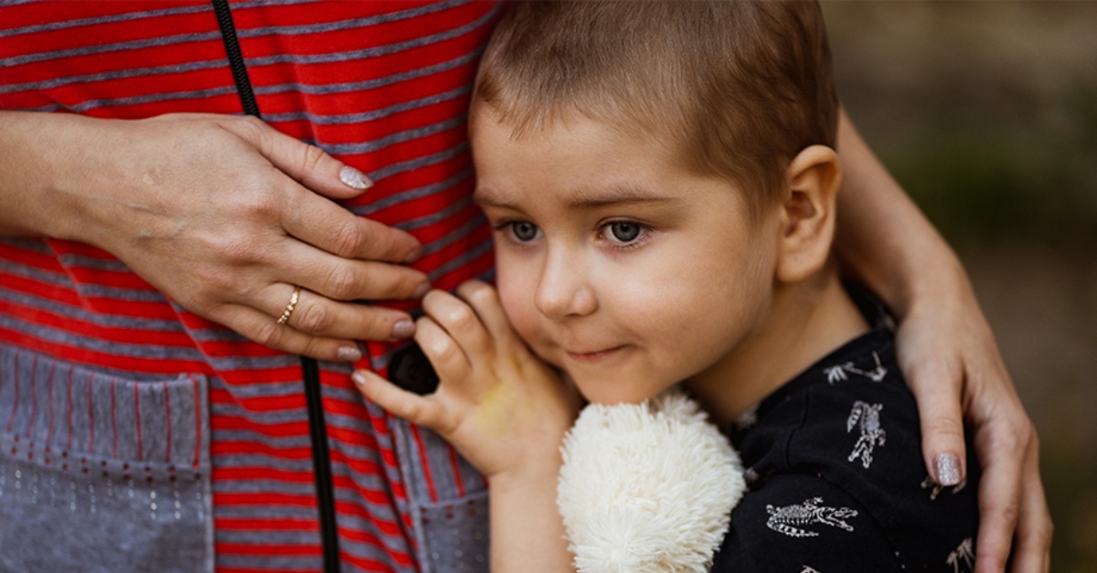 A young child hugs their mother's waist and holds a stuffed animal. Corporate social responsibility refugees